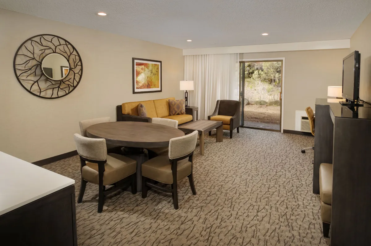 An inviting open-plan area showcasing a round dining table, a comfy sofa seating zone, decorative wall art, a mirror, and a patio door leading outside. The setting suggests warmth, connectivity, and the option for relaxation or communal dining.
