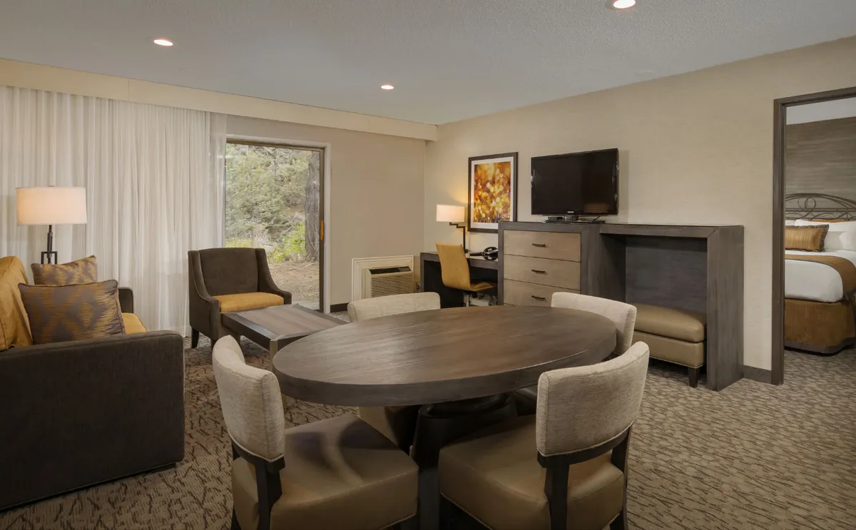 A spacious living area featuring a comfortable sofa, dining table, television, and a window. The arrangement encourages both relaxation and productivity, with ample space for family gatherings or working from the room.